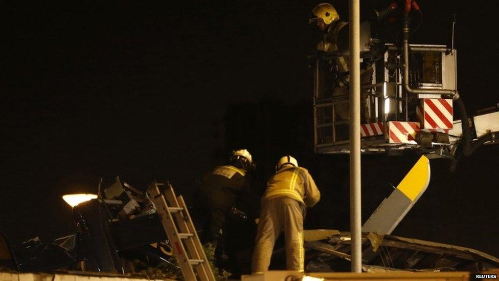 Two firemen working on the roof of a pub where a helicopter crashed. Another fireman is on a platform above them