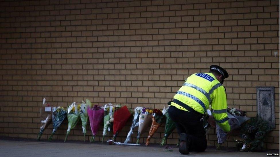 A police officer lays a bunch of flowers against a wall where more bunches of flowers have already been placed