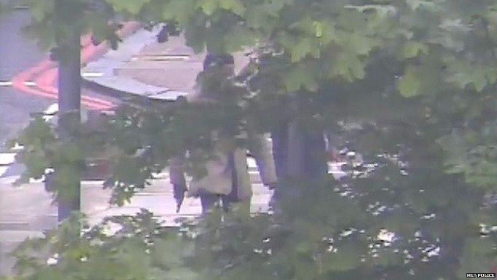 Michael Adebowale with gun in right hand behind tree