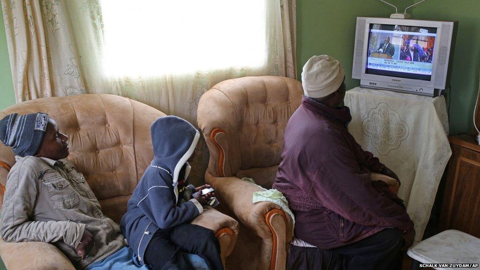 Ndzondzo Mabope sits with family members as they watch a local television station broadcasting live images from former president Nelson Mandela memorial held in Johannesburg