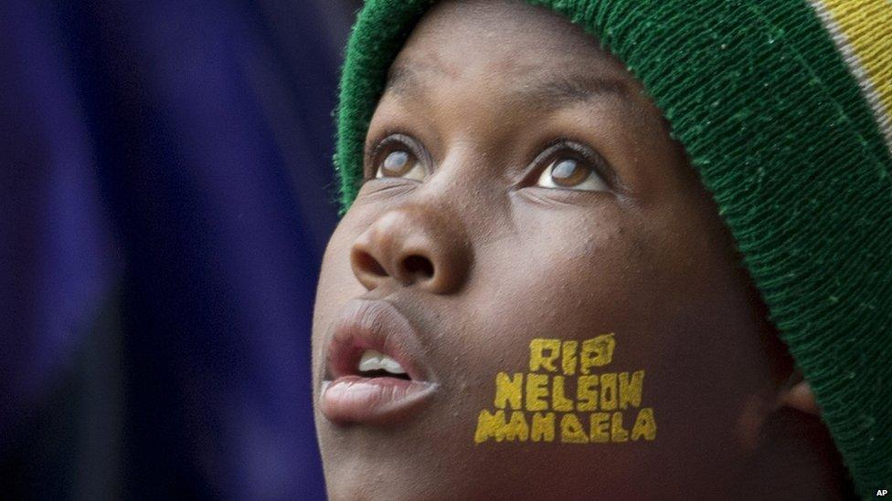 A boy with "Rest In Peace Nelson Mandela" painted on his face looks up to the skies during the memorial service.