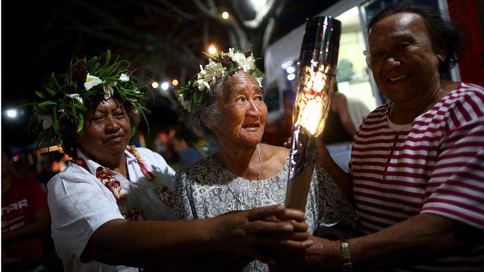 Members of the local community hold the Queen's Baton at a local beach market in Rarotonga, Cook Islands.