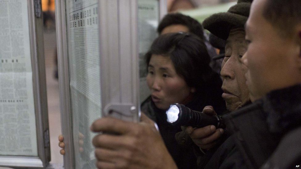 A North Korean man uses a flashlight as he and other subway commuters gather around a public newspaper stand on the train platform in Pyongyang, North Korea on 13 December 2013