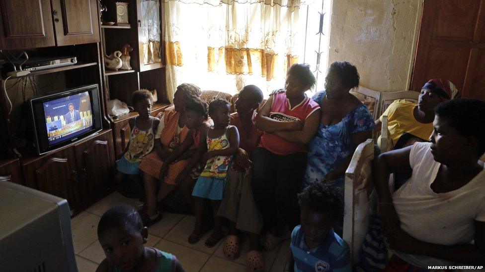 A family watch a television showing the funeral service of former South African President Nelson Mandela at their home in the Soweto, Johannesburg