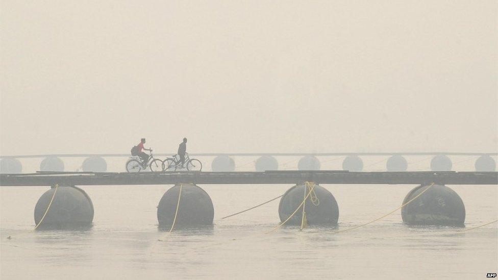 Indian residents ride bicycles as they cross a pontoon bridge during a foggy day in Allahabad on December 23, 2013.