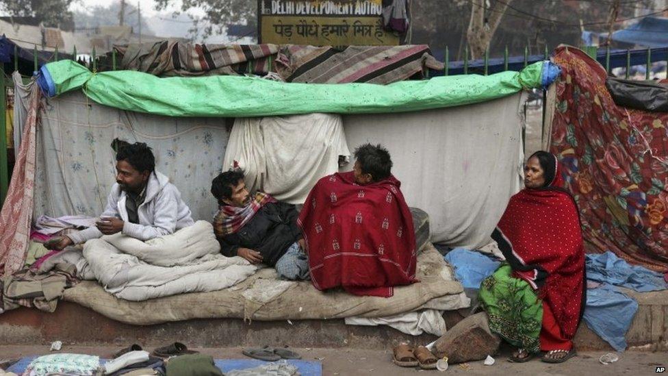 Indian homeless people sit wrapped in woollen clothes outside their makeshift shelter on a cold winter morning in New Delhi, India, Sunday, Dec. 22, 2013.