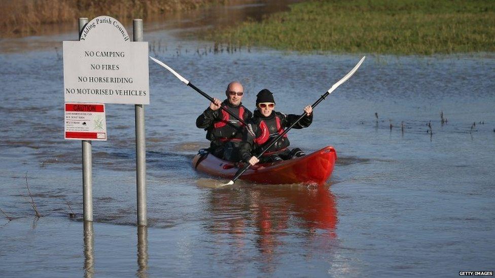 A woman and a man paddle a kayak on flooded land