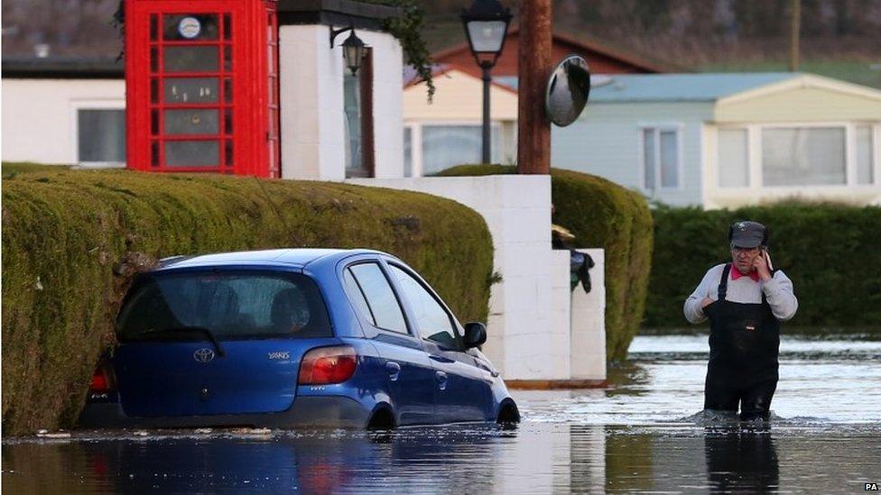 A man speaks on the phone while standing in knee-deep flood water