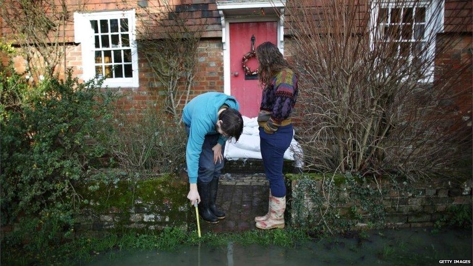 A man uses a stick to test the depth of water outside a house