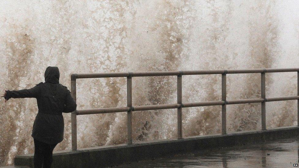 A woman standing by the sea as waves batter the shore