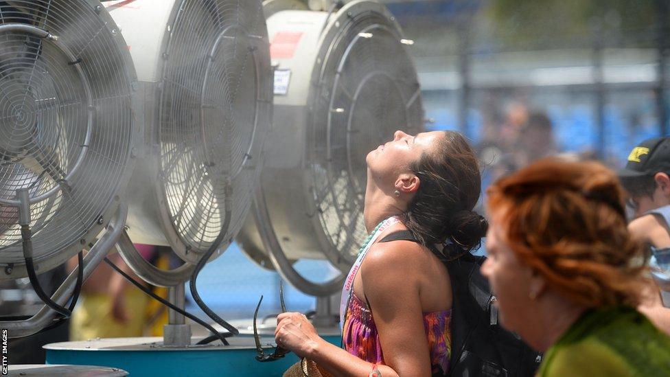 A woman cools off with fans and mist put out for spectators as a heat wave continues to sizzle on day three of the Australian Open