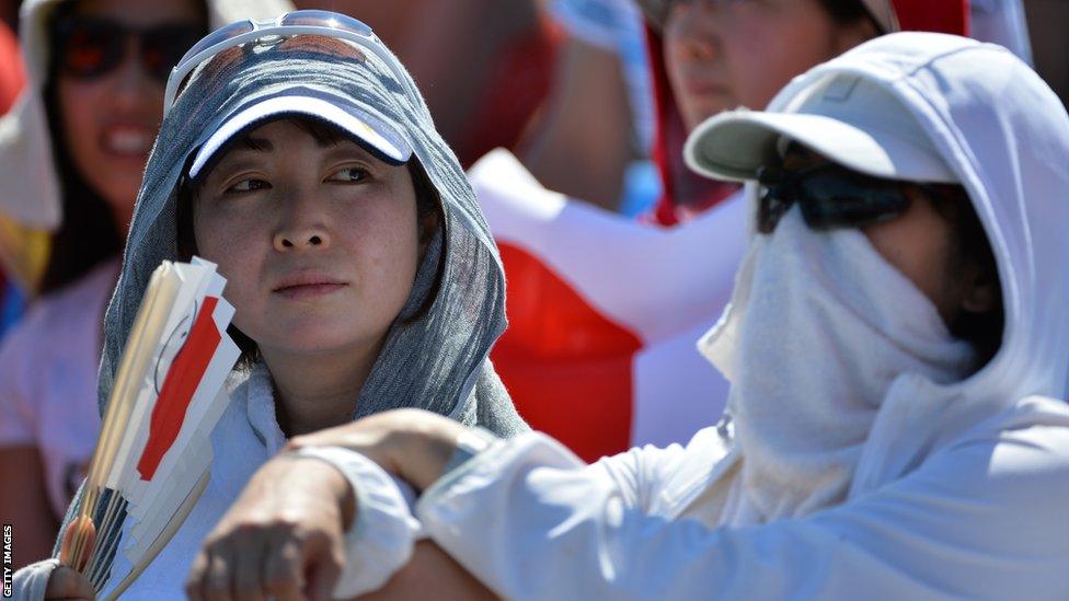 Spectators cover up to beat the heat as they watch Japan's Kei Nishikori