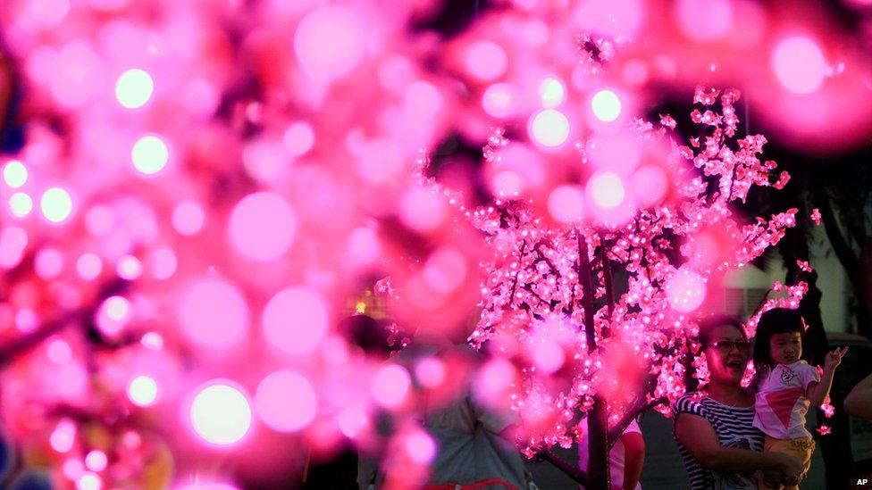 People pose for photos around artificial cherry blossom trees with LED lights on display for the upcoming Chinese new year in Kuala Lumpur, Malaysia