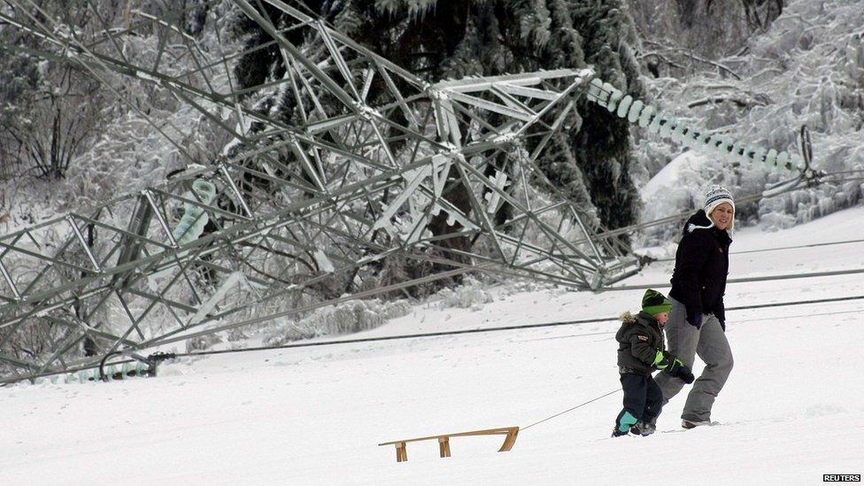 A woman and child walk past a fallen pylon with a sledge.