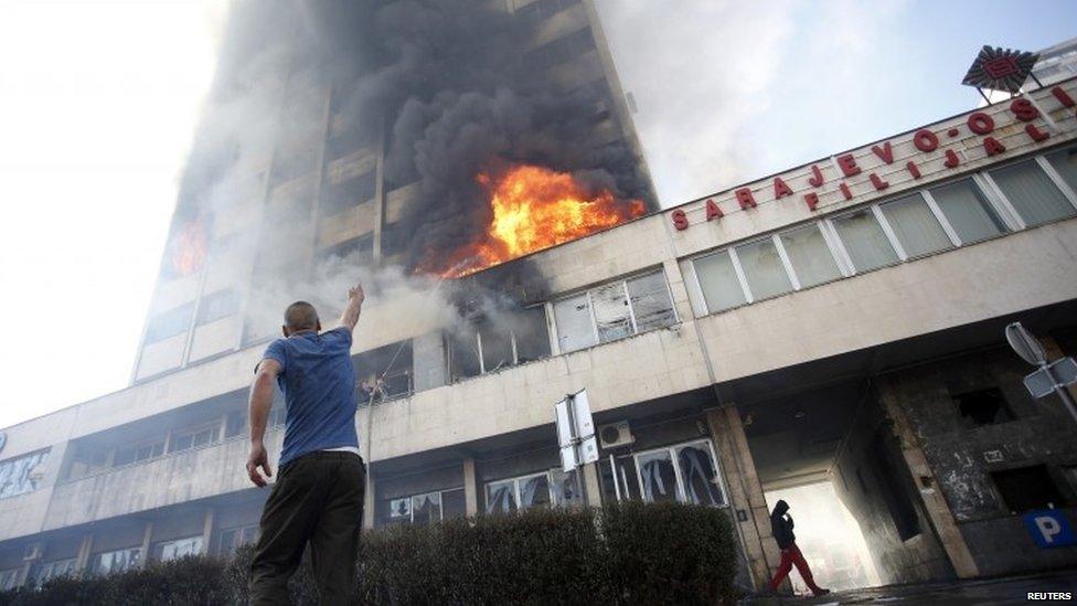 Man stands outside a burning government building in Tuzla (7 February 2014)