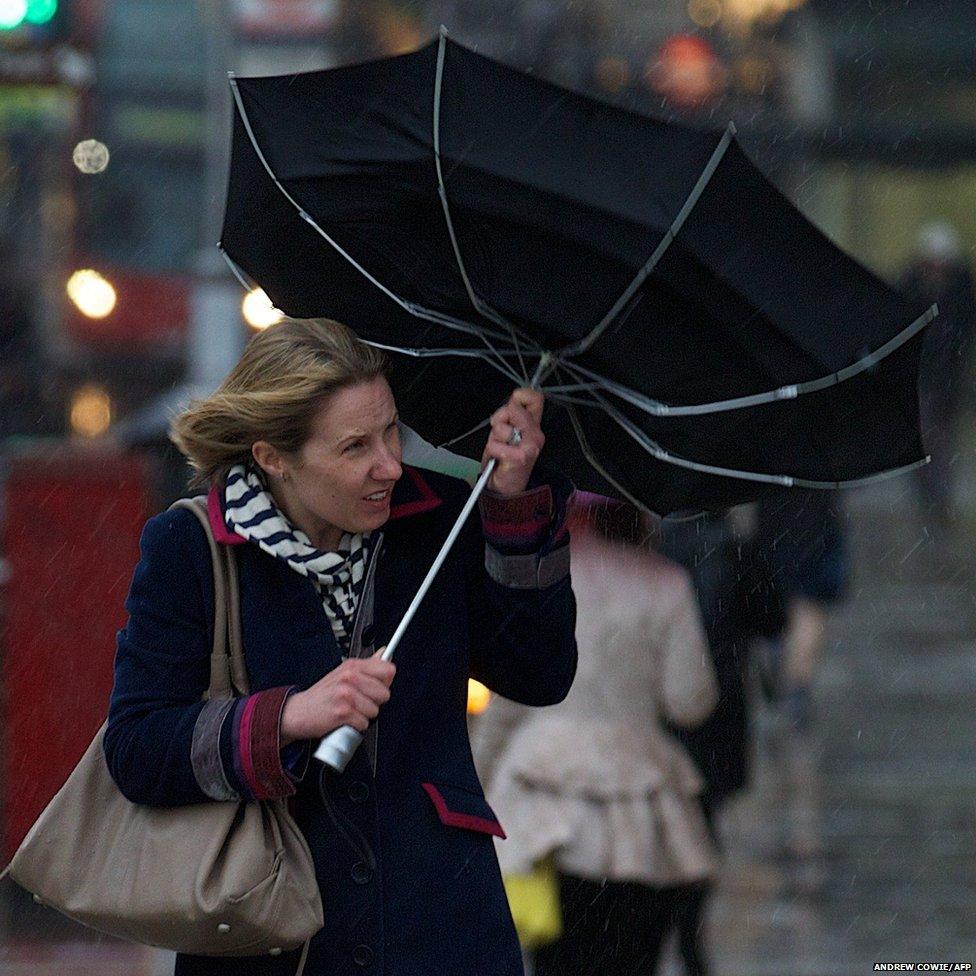 A woman battles the high winds with her umbrella as she walks across a bridge in central London