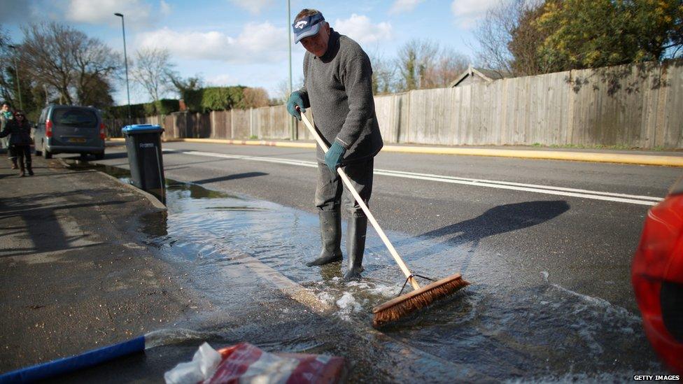 A man attempts to brush flood water away from the front of his house in Chertsey, England