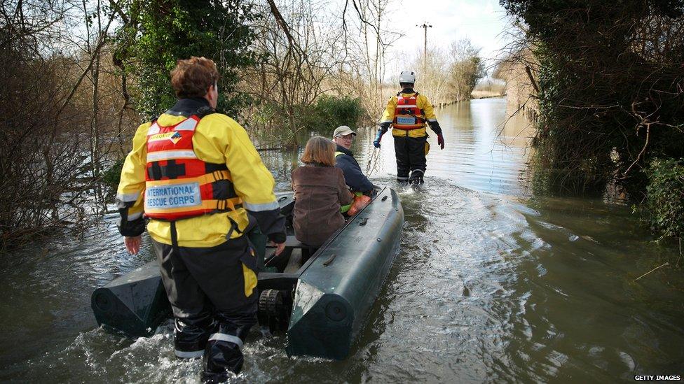 Volunteers from the International Rescue Corps help a couple evacuate from a flooded house in Chertsey