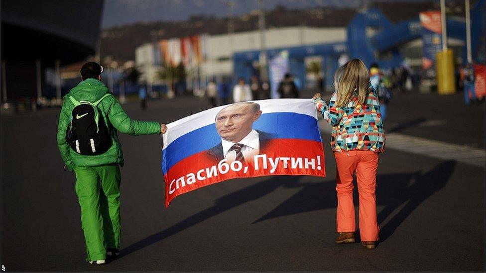 A Russian flag with the message "Thank you, Putin!" written across it is carried through the Olympic Park ahead of the closing ceremony