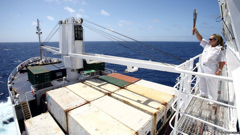 RMS St. Helena Second Officer Mia Henry holds the Queen's Baton aloft looking out over the RMS St. Helena during its 5-day voyage from Cape Town, South Africa to St. Helena