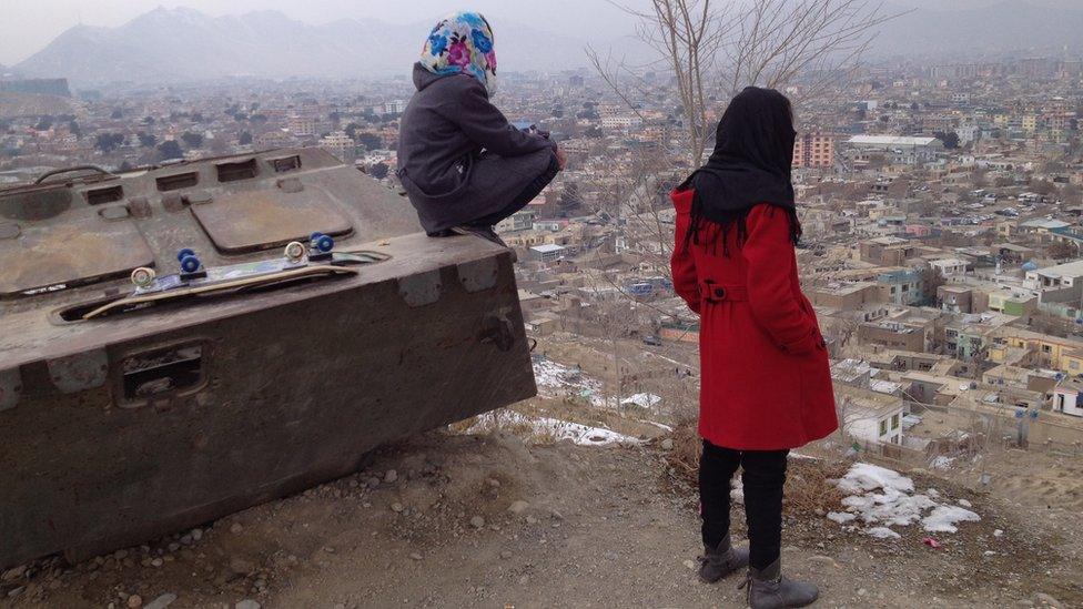 Girls with skateboards look out over Kabul