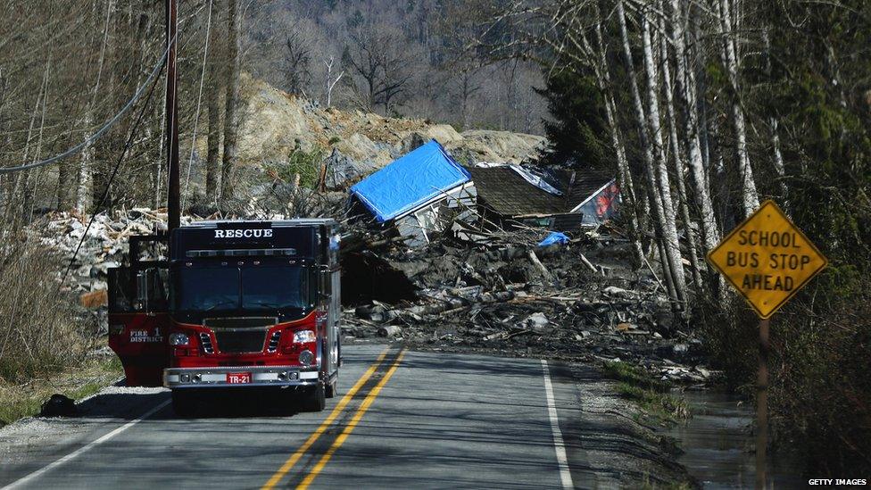 A road blocked by buildings uprooted and pushed down a hill by the landslide