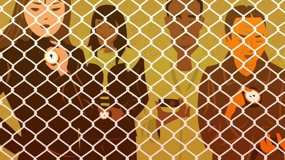 People stand behind a chain-link fence.