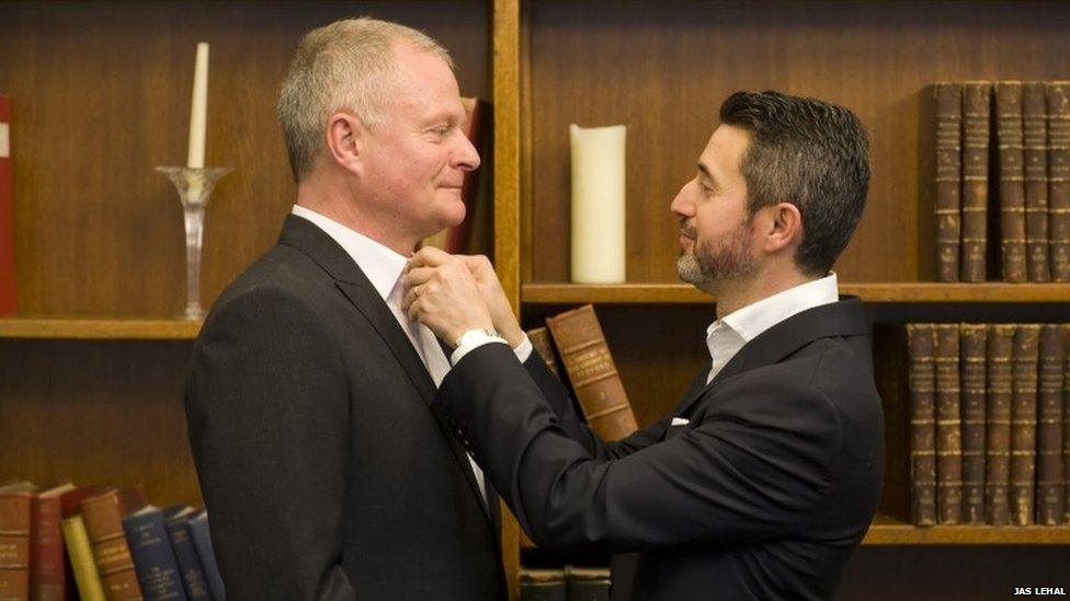 A man adjusts the shirt collar of another man