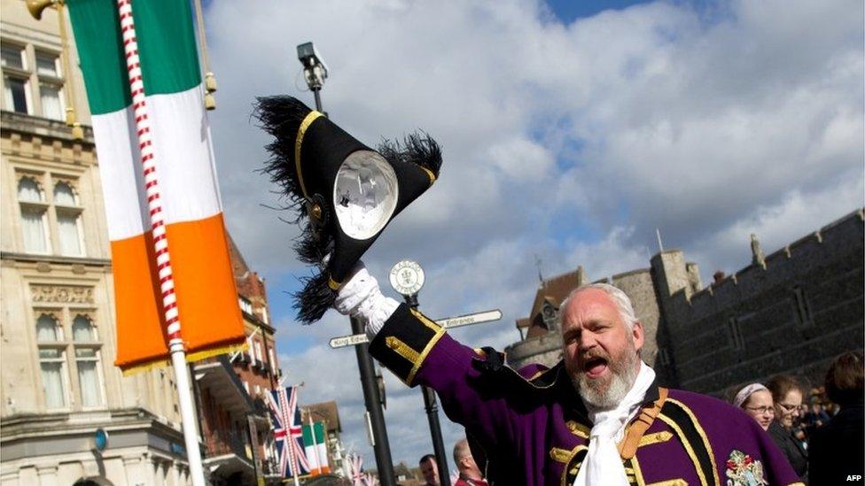 A town crier shouts and waves his hat