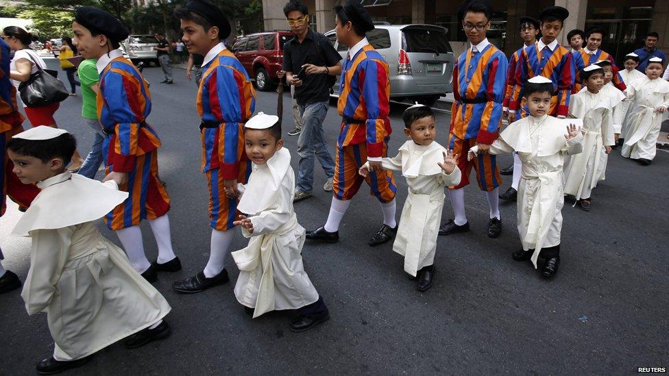 Children wearing Pope's cassocks cross a road before taking part in a parade in Quezon city, Metro Manila April 27