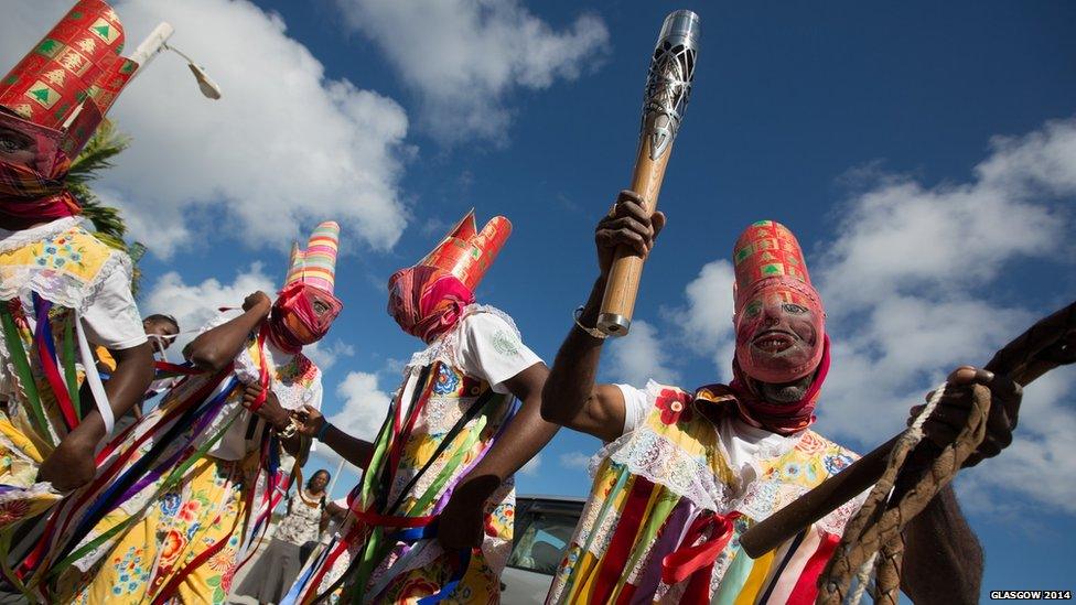 A group of masked dancers, one of whom holds the Queen's Baton.