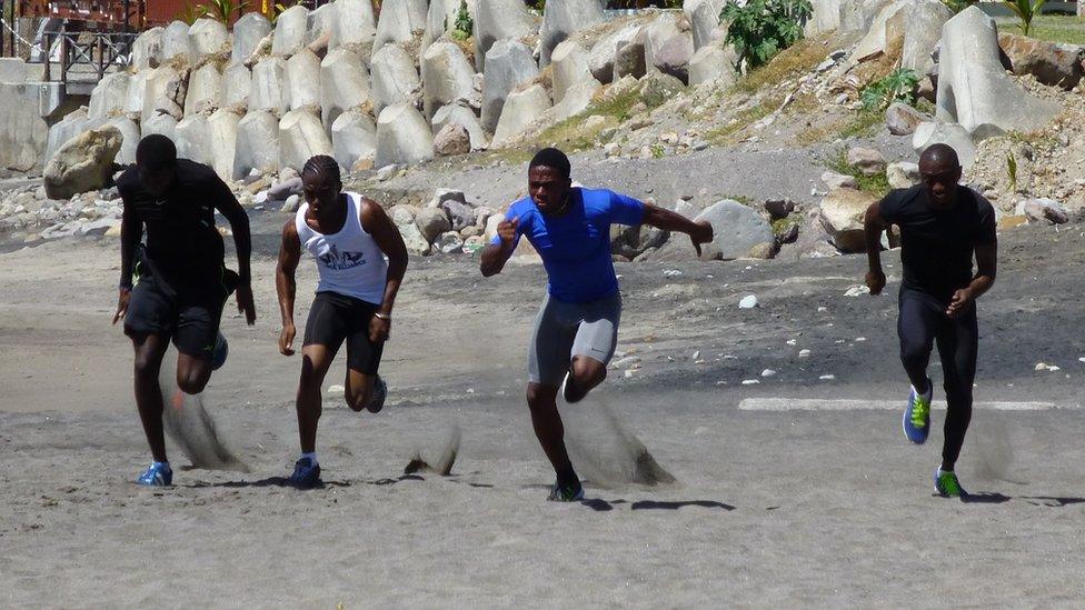 Four men running on sand.