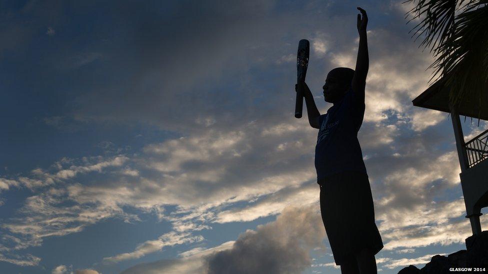 Silhouette of a child holding the Queen's Baton aloft.