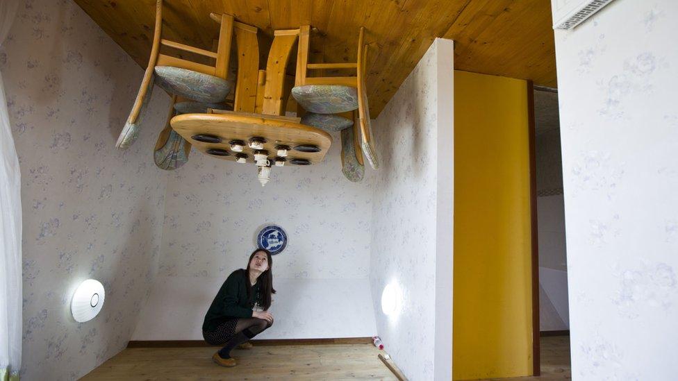 Woman poses in upside-down house.