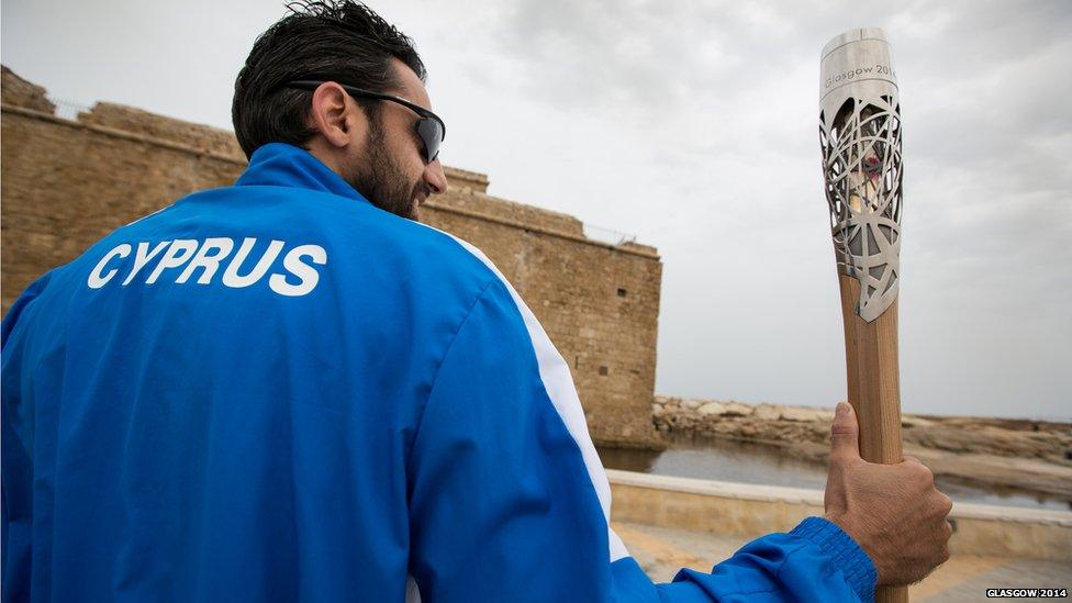 Man in a Cyprus team tracksuit holding the Queen's Baton.