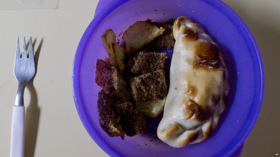 A plastic plate containing an empanada of meat, milanesa (meat covered with egg and bread), and potato is set on a table where children ages 2 to 5 years old have lunch at a school in Buenos Aires, Argentina.