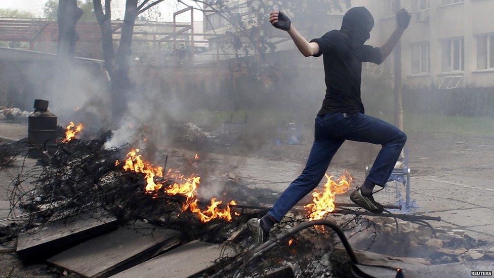 A masked man jumps over a burning barricade in front of the police headquarters in the south-eastern port city of Mariupol, 9 May 2014