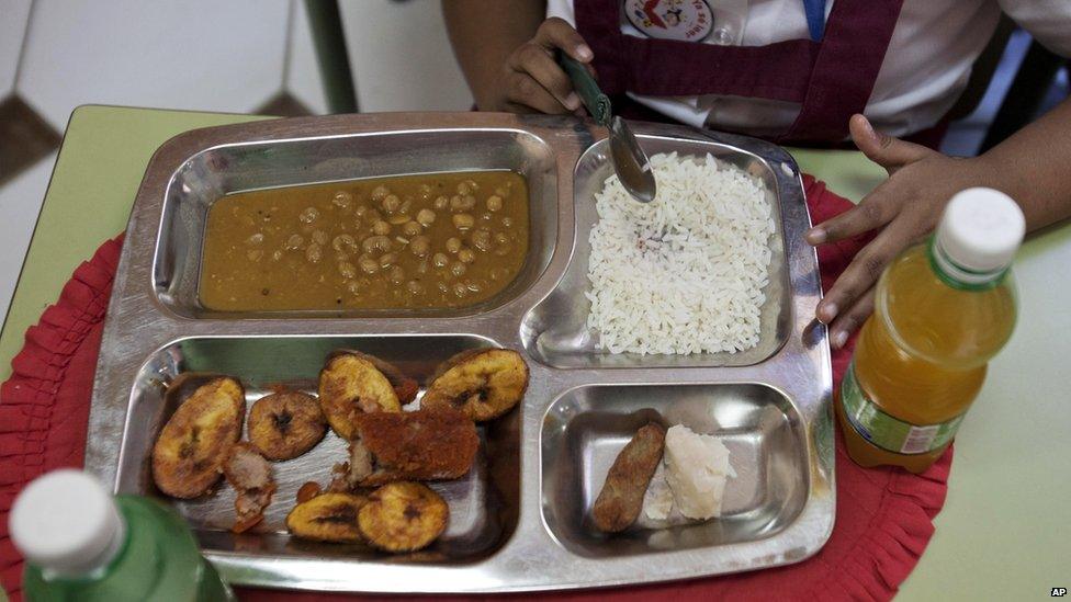 Milagro Ramos, a student at the Angela Landa elementary school, spoons up rice from her lunch tray, which also contains a chicken croquette, a piece of taro root and yellow pea soup in Old Havana, Cuba. Milagro brought fried plantains, lower left corner of her tray, and an orange drink from home. The children provide their own drinks.