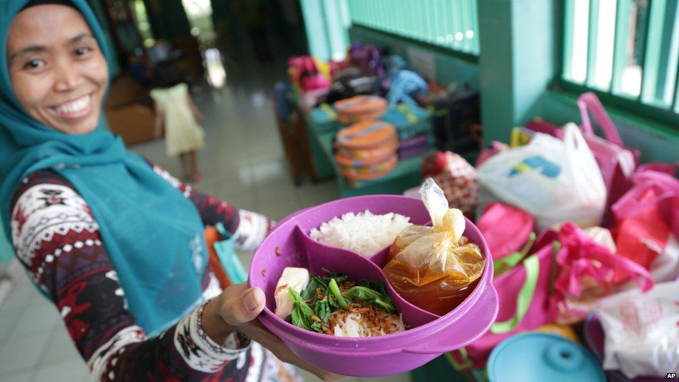 Sri, a house maid, shows a lunch box she prepared for her employer's child, at an elementary school in Jakarta, Indonesia. The lunch consists of rice, meatball soup, and tofu and vegetables.