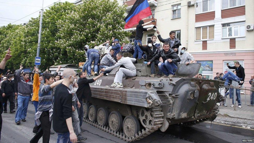 People climb a broken armoured vehicle left behind after Ukrainian forces attacked police headquarters in an attempt to drive out pro-Russian militants in Mariupol, 9 May 2014