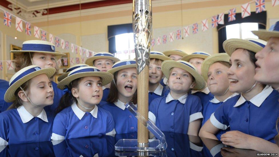 Schoolgirls wearing straw hats look at the Queen's Baton.