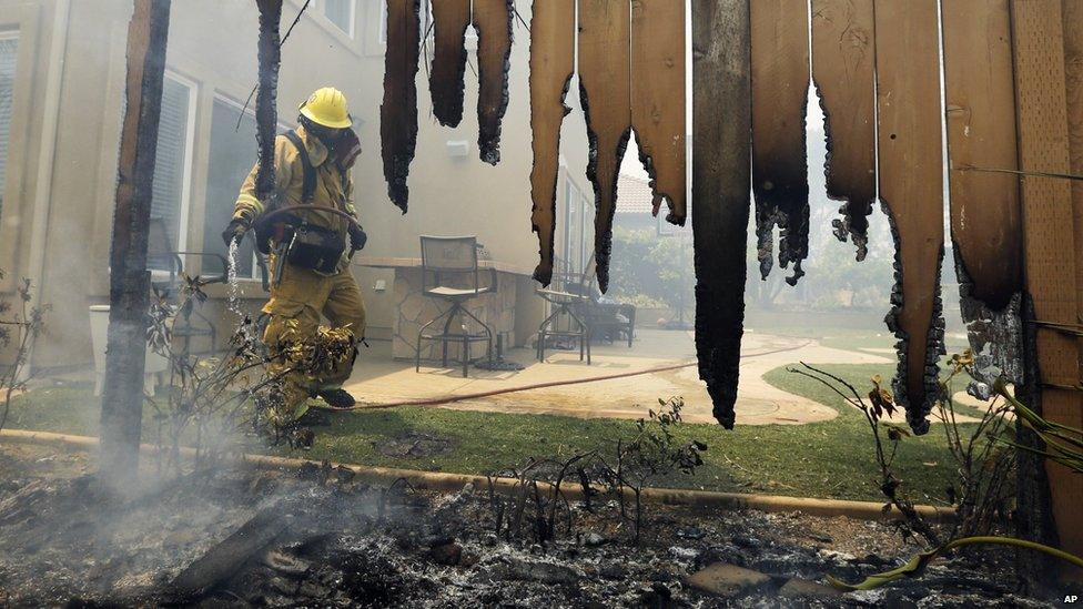 A firefighter put water on a house fence during a wildfire in Carlsbad, California, on 14 May 2014