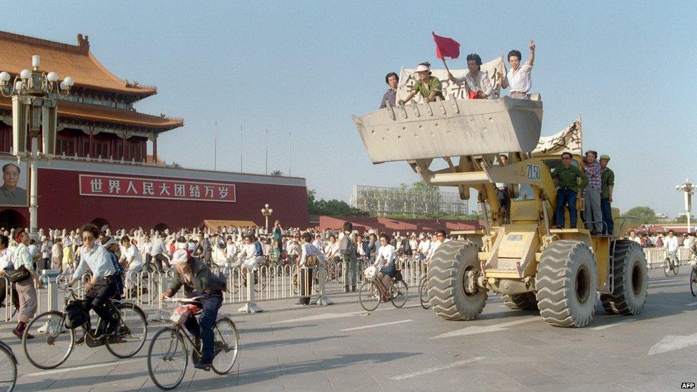 Workers sit in a bulldozer shovel, shouting slogans as they drive their engine in front of the Forbidden City in Tiananmen Square on 25 May 1989