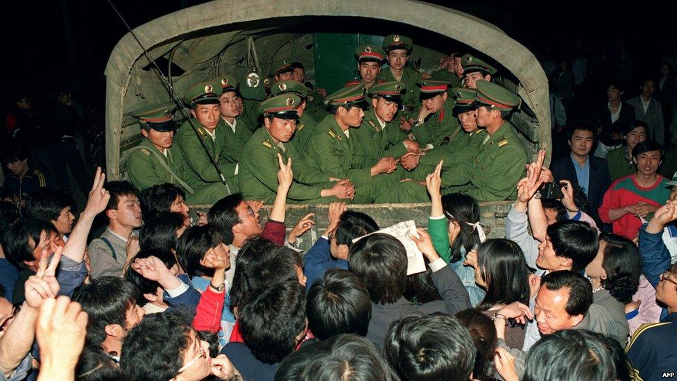 Pro-democracy demonstrators raise their fists and flash "victory" signs as they stop a military truck filled with soldiers on its way to Tiananmen Square