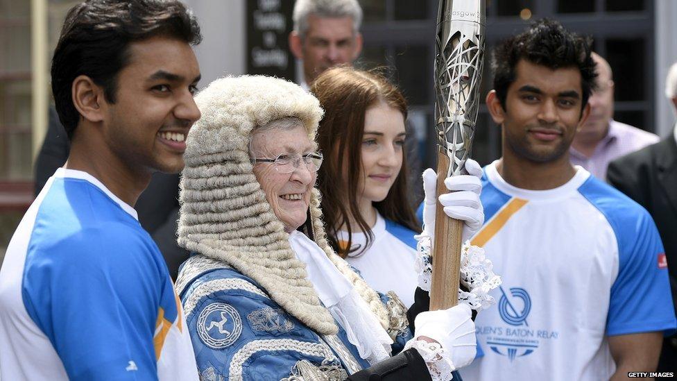 President of Tynwald Clare Christian holds the Queen's Baton flanked by young athletes