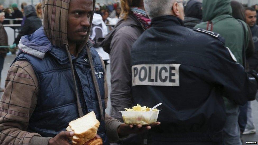 An Eritrean migrant walks past a police officer during the daily food distribution at the harbour in Calais