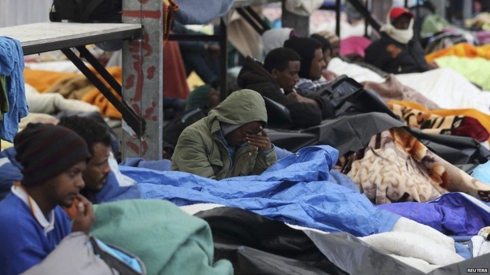 Eritrean migrants rest under blankets in the courtyard at a food distribution centre after they fled their makeshift camp to find shelter in Calais