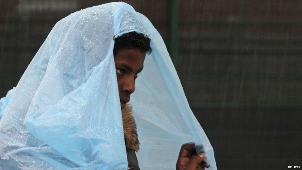 An African migrant shelters from heavy rain under a a bag during the daily food distribution at the harbour in Calais