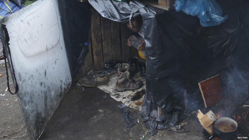 A migrant protects himself from the rain in the middle of makeshift shelters at the harbour in Calais