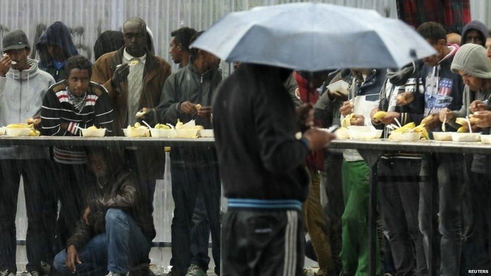 Migrants try to shelter from heavy rain during the daily food distribution at the harbour in Calais